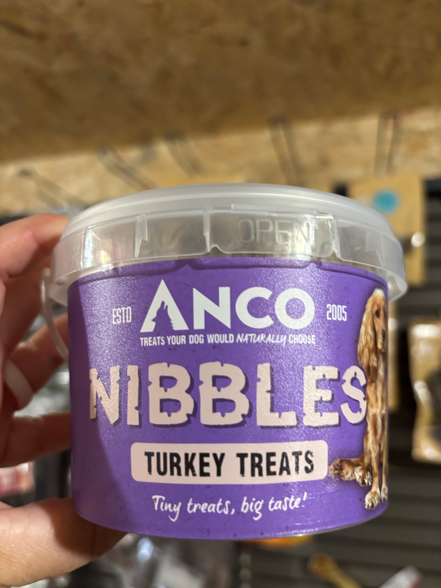 Container of Ancol Nibbles Turkey Treats held by a person with a blurred background